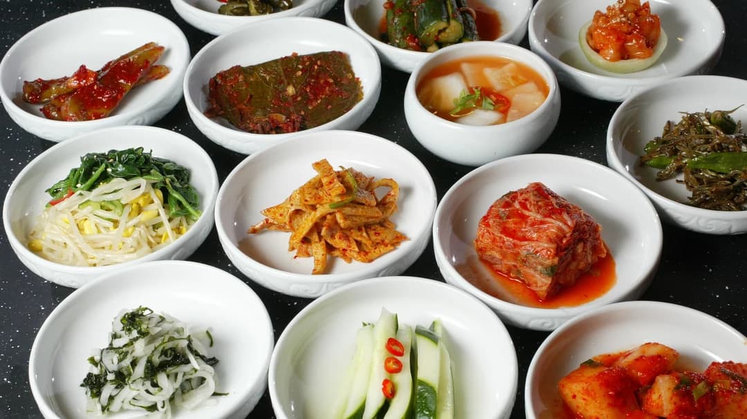 Small white bowls of seasoned banchan side dishes arranged in rows